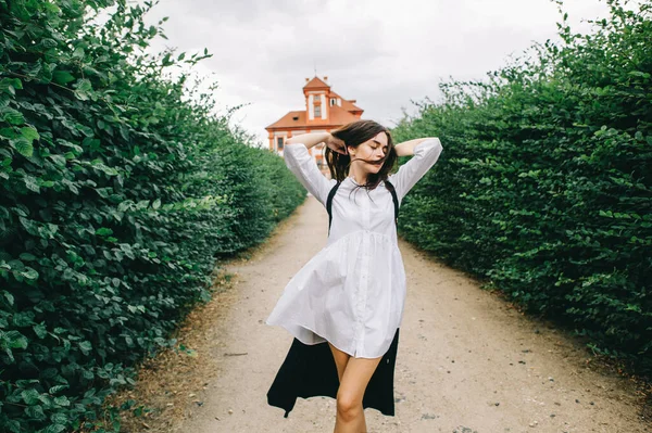赤の宮殿の背景にある緑の路地を歩いている若い白人のスタイリッシュな女の子 — ストック写真