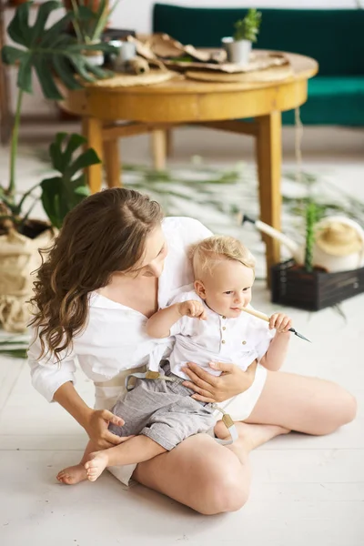 若いです美しいですお母さん遊び彼女の赤ちゃんと床の上に木のテーブルの近くに植物と緑のソファ — ストック写真