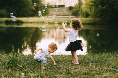 Yakışıklı genç baba ve güzel anne güneşli yaz doğasında sevimli küçük çocuklarıyla oynuyorlar.