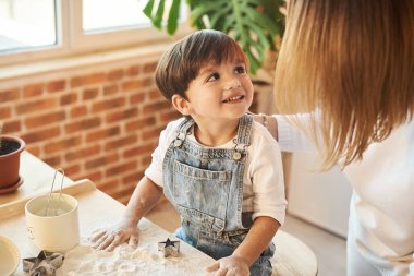 Genç ve güzel bir aile güneşli mutfakta eğleniyor ve yemek pişiriyor.