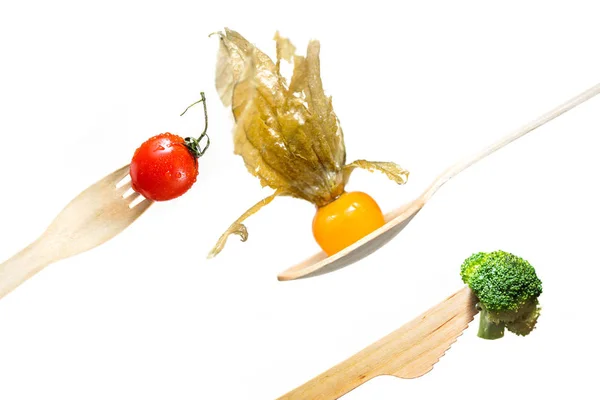 Fresh vegetables tomato, broccoli, physalis on wooden fork, knife, spoon — Stock Photo, Image