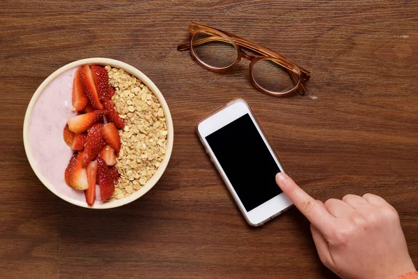Bowl of muesli and smartphone on a wooden table.