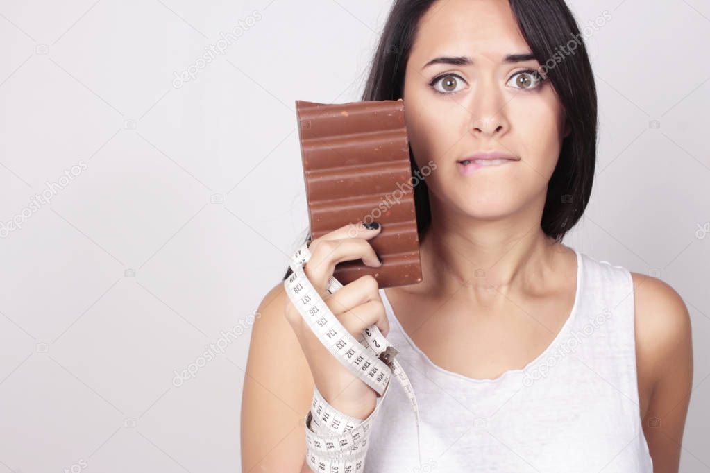 Young woman deciding holding chocolate and measure tape