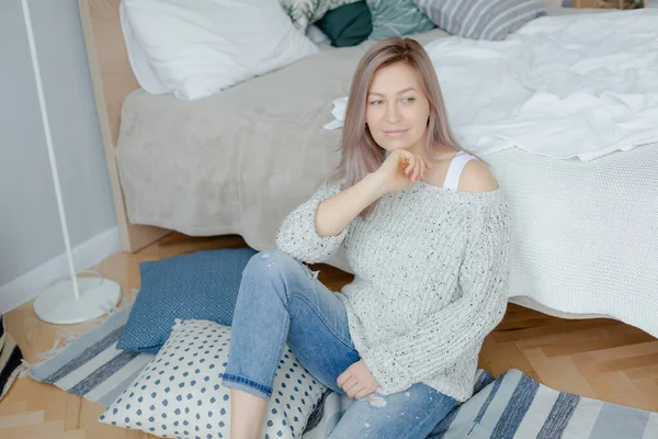 Mujer joven rubia en jersey gris está cerca de la cama — Foto de Stock