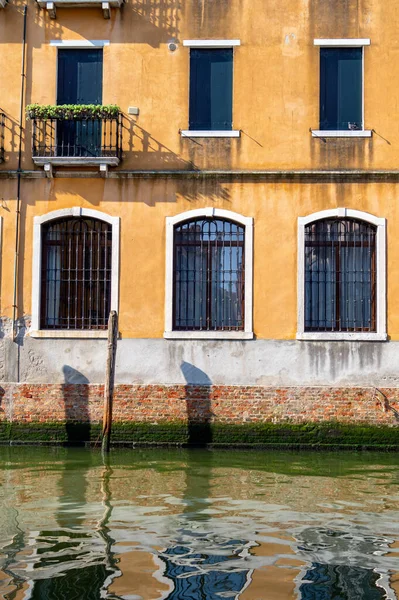 Venice, Italy. Windows of old yellow house are reflected in green water of canal — Stock Photo, Image