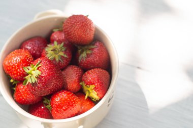 Beyaz ahşap masada bir kasede olgun çilekler.