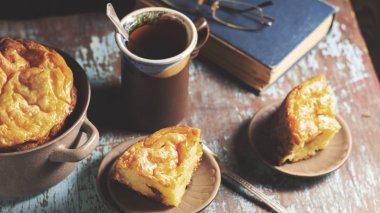 Süzme peynir güveci, bir fincan çay ve ahşap bir masada yün bir eşarp.