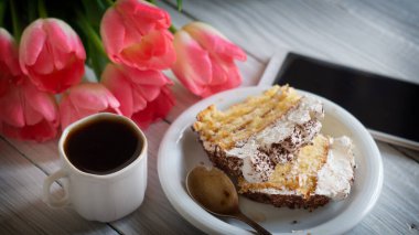 Tiramisu keki, pembe laleler ve beyaz tahta bir masada bir fincan kahve.