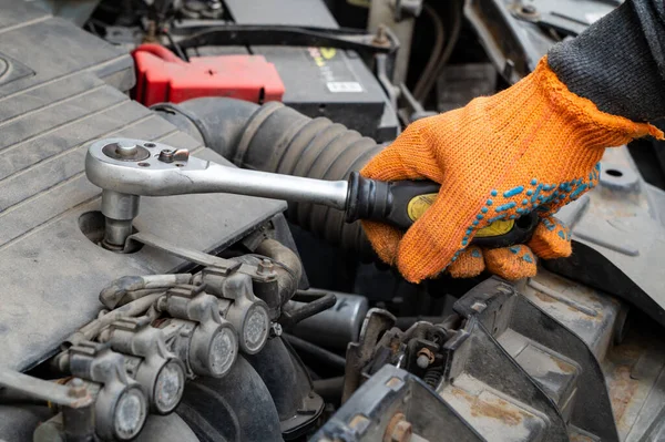 Koruyucu eldivenli erkek tamirci İngiliz anahtarıyla arabanın motorunun vidasını sökmüş.