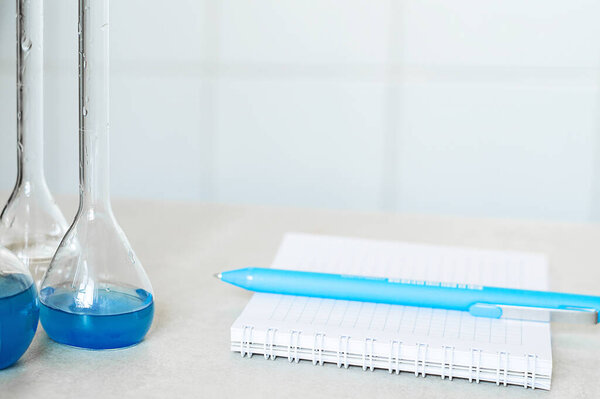 Reagents in flasks, a notebook and a pen on a table in a chemical laboratory