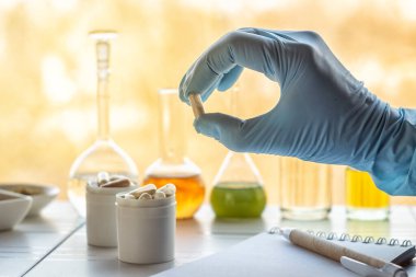 Bir eczacının elinde laboratuardaki malzeme kavanozlarının arka planında beslenme takviyeleri olan bir kapsül bulunur.