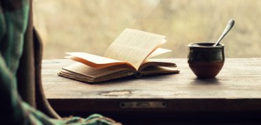 Bir fincan kahve ve ahşap pencere pervazında açık eski bir kitap. Retro styl