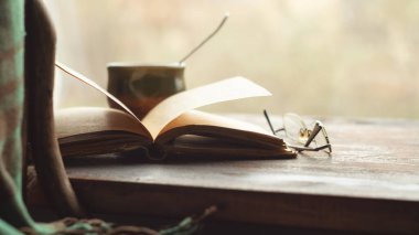 Bir fincan kahve, eski kitap ve bardaklar pencere eşiğinde, ekoseli bir sandalyenin yanında. Retro biçimi