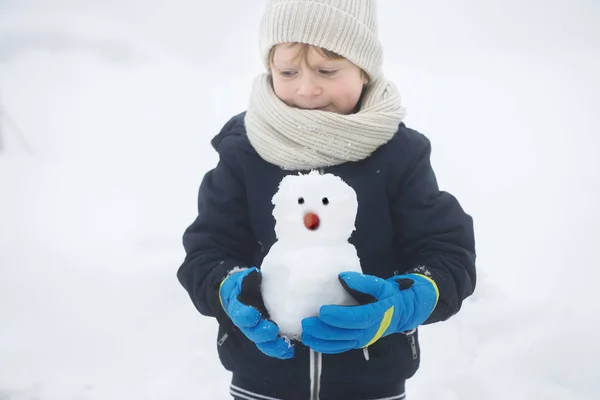 Un niño feliz en invierno con un muñeco de nieve en las manos —  Fotos de Stock
