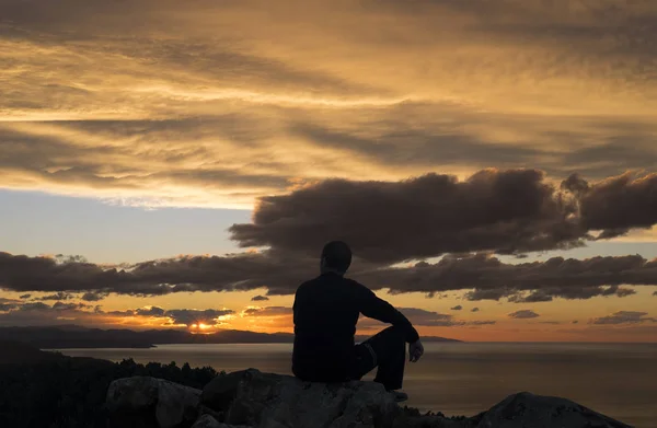 看着大海和夕阳的人坐在岩石上 — 图库照片