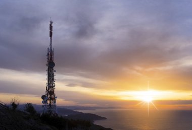 telecommunication tower with the sun as it beats over the sea clipart