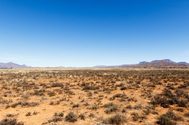 Barren field with mountains and blue sky clipart