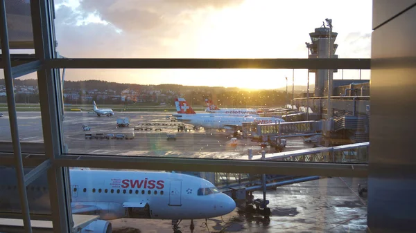 ZURICH, SUÍÇA - MAR 31, 2015: Vista do aeroporto através da janela da área de espera - aviões da companhia aérea SWISS em uma fileira nos portões durante a luz do sol — Fotografia de Stock