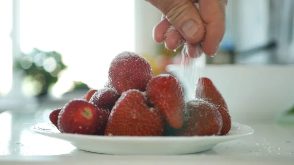 Man hand sätta vitsocker över en tallrik full med röda jordgubbs frukter — Stockfoto