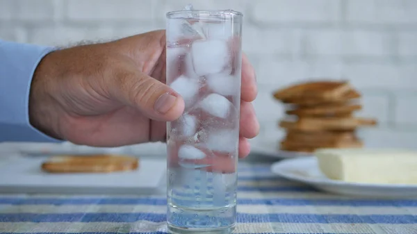 Homem tirando da mesa um copo com cubos de gelo e água doce — Fotografia de Stock