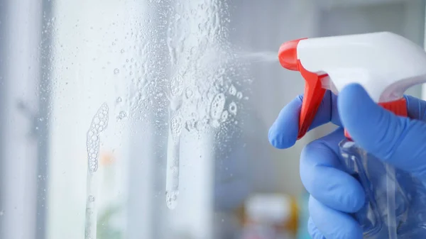 Close Up Hombre Manos con guantes azules Limpieza de una ventana con líquido pulverizado — Foto de Stock
