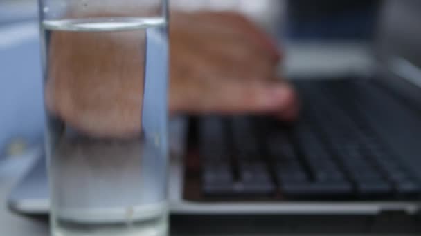 Человек со стаканом воды на столе завершает свою работу и закрывает лап — стоковое видео