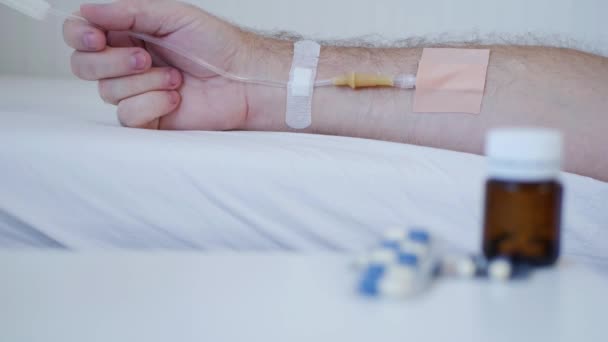 Страждаюча людина в лікарні з медичною перфузією в руці і таблетками розмиті — стокове відео