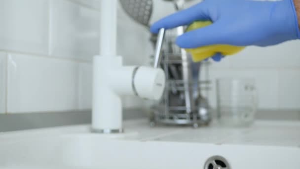 Руки с резиновыми перчатками открытого крана воды и промыть блюдо губкой в раковине — стоковое видео
