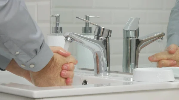 Image with a Man in Apartment Bathroom Washing His Hands in a Ceramic Sink