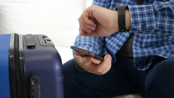 Mann mit Koffer wartet Transportkontrolle Zeit auf seiner Handuhr und Text mit einem Handy — Stockfoto