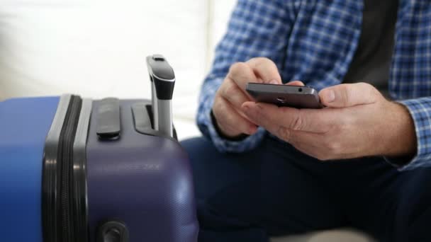 Homem viajando em texto de férias usando um telefone celular, pessoa com smartphone na mão esperando perto de uma mala — Vídeo de Stock