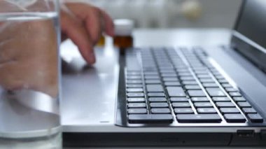 Hasta Adam, masadaki su ve ilaçlarla dizüstü bilgisayar kullanıyor.