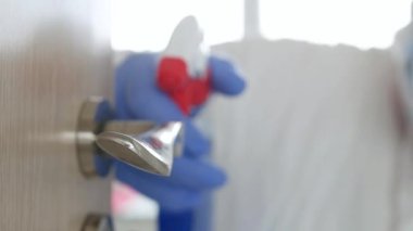 Ağır çekim adamı koruyucu giysi, eldiven, maske ve gözlük takıyor. Hastane karantinasında antibakteriyel çözümle dezenfekte edilen kapı kolu.