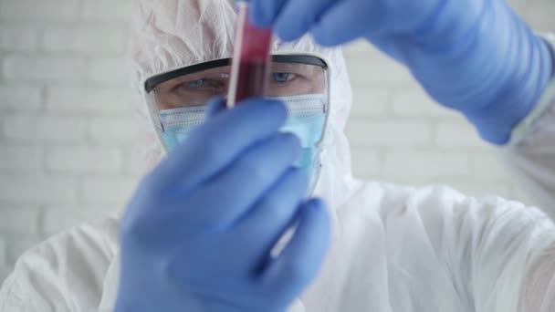 Movimento lento com um médico no laboratório do hospital vestindo um terno de proteção olhando para um tubo com sangue infectado com coronavírus — Vídeo de Stock