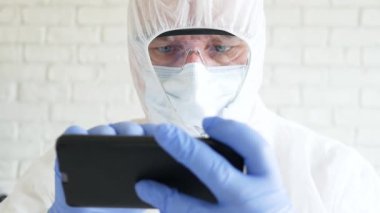 Hastanedeki Karantinada Koruyucu Takım Elbise, Eldiven, Maske ve Gözlük Giyen Bir Doktorla Yavaş Hareket Cep Telefonu Kullanarak