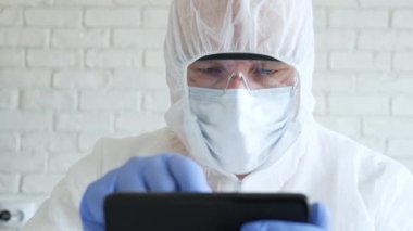 Hastane Karantinasında Koruyucu Takım Elbise, Eldiven, Maske ve Gözlük Giyen Doktor Cep Telefonu Kullanarak