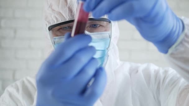 Doctor in Hospital Laboratory Wearing a Protection Suit Looking to a Tube with Blood Infected with Coronavirus — стокове відео