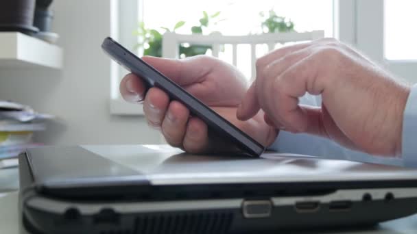 Επιχειρηματίας Χρησιμοποιώντας ένα κινητό τηλέφωνο SMS και εργασίας σε απευθείας σύνδεση από το σπίτι, ο άνθρωπος πρόσβαση σε μια σύνδεση στο διαδίκτυο με το γραφείο από το τηλέφωνο και το laptop — Αρχείο Βίντεο
