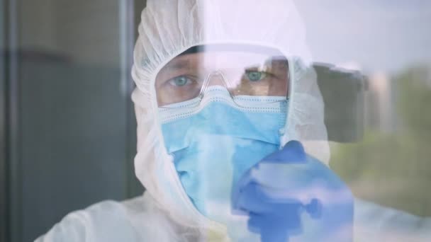 Médico con traje de protección, máscara facial, gafas y guantes para aislamiento COVID-19 en la parte posterior de una ventana en una habitación de hospital — Vídeos de Stock