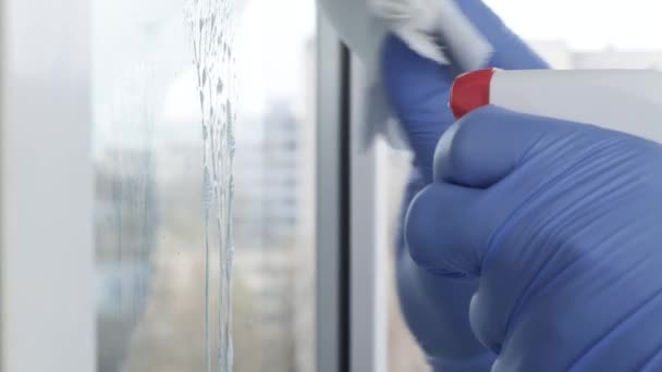 Закройте руки человека в голубых перчатках, очищая окно с помощью опрыскиваемой жидкости для дезинфекции вирусов — стоковое видео