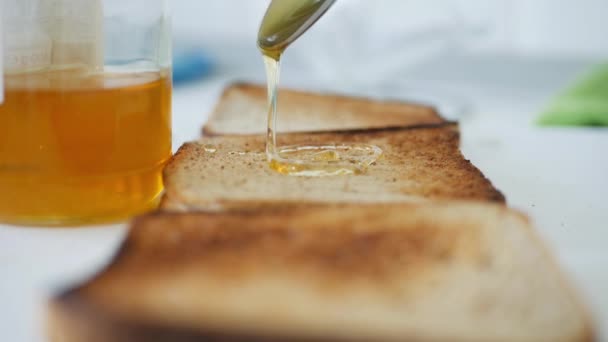 's Ochtends ontbijt met een man die zoete honing op de toast strooit, verse honing op een sneetje brood in de keuken in slow motion — Stockvideo