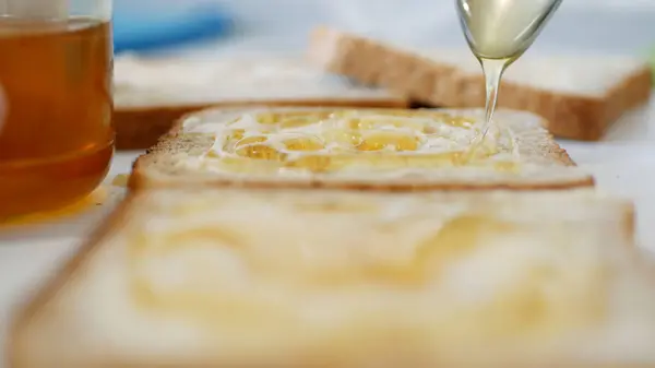 Colazione mattutina con uomo che spalma miele dolce sul pane tostato, miele fresco su una fetta di pane in cucina — Foto Stock