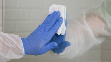 Koruyucu giysiler giyen, tuvalette aynayı dezenfekte eden, karantina altındaki bir hastanedeki tuvaletin içini temizleyen...