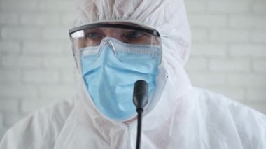 Korunma giysisi giyen ve COVID-19 salgınıyla ilgili bir basın toplantısında konuşan doktor.
