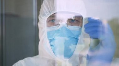 Doktor Koruyucu Takım Elbise, Yüz Maskesi, Gözlük ve Bir Hastanedeki Pencerenin Arkasında COVID-19 İzolasyonu İçin Eldiven Giyiyor