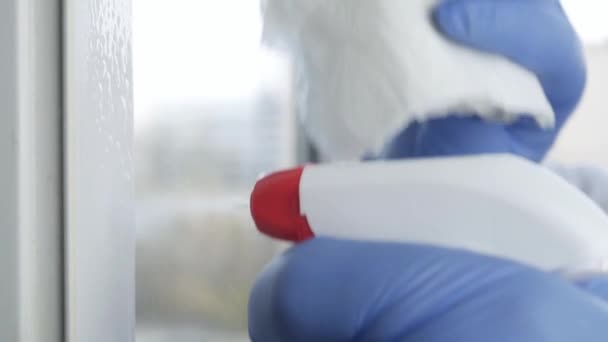 Людина з повільним рухом руки з блакитними рукавицями чистить вікно за допомогою розпорошеного рідини дезінфекція проти COVID-19 Забруднення — стокове відео