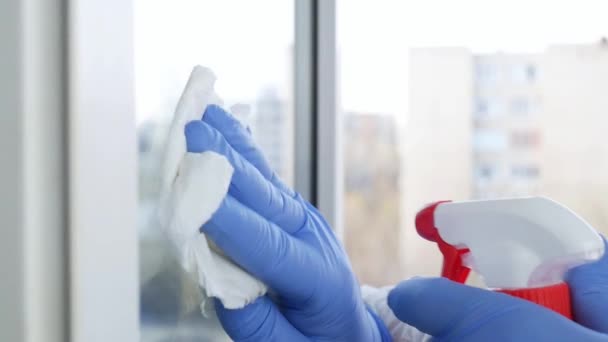 Mani dell'uomo di rallentamento con i guanti blu che puliscono una finestra usando la disinfezione liquida spruzzata contro la contaminazione COVID-19 — Video Stock