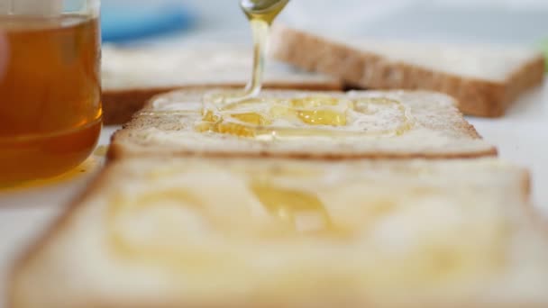 Desayuno por la mañana con el hombre esparciendo miel dulce en el brindis, miel fresca en una rebanada fresca de pan en la cocina — Vídeo de stock