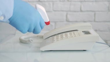 Ellerinde koruma eldivenleri olan, sprey ve ıslak mendil kullanarak telefonu temizleyen ve dezenfekte eden bir adamla Yavaş Hareket