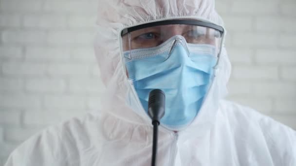 Homem da medicina vestindo um terno da proteção e conversando em uma conferência de imprensa médica sobre a pandemia de COVID-19 — Vídeo de Stock